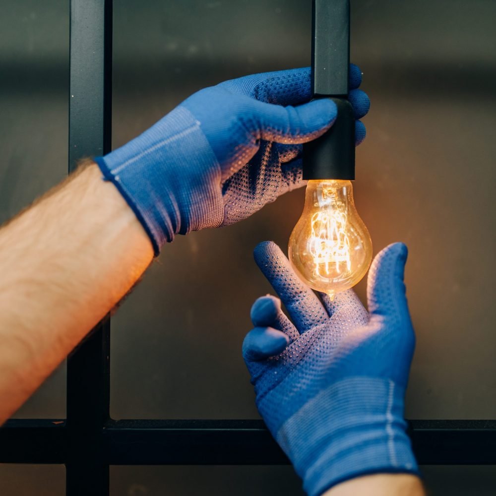 Electrician in uniform replaces the light bulb, handyman. Professional worker makes repairs around the house, home repairing service